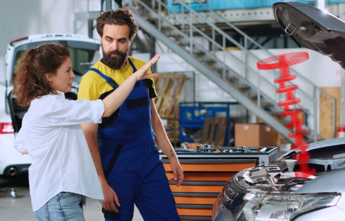 Serviceman in car service using holographic augmented reality to show customer defective vehicle piston. Hardworking garage employee using innovative AR tech to project automobile parts for woman