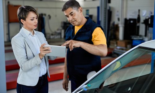 Car mechanic and female manager cooperating while working on touchpad in auto repair shop.