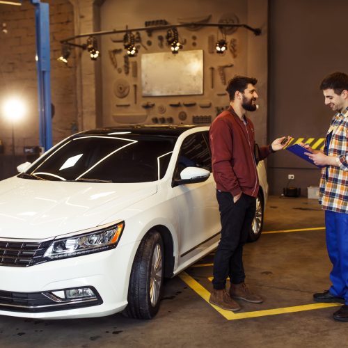 male customer in auto service center explaning the problems of his car to mechanic with clipboard, sun effect